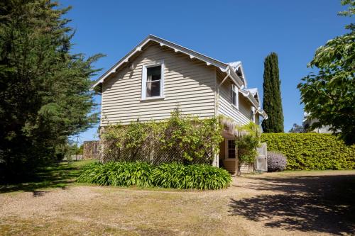 an old white house with trees and bushes at Craignair Cottage in Mount Macedon