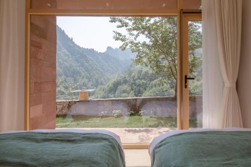 a bedroom with a large window looking out at a mountain at Vretreats Suyunjian Boutique Hotel in Xinglong