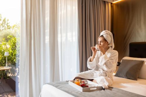 a woman in a robe sitting on a bed eating food at Boutique Hotel Sirmione in Sirmione