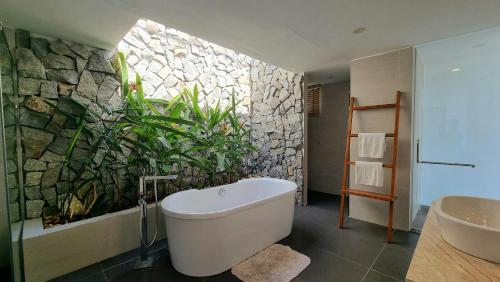 a bathroom with a large white tub and a stone wall at Anh Nguyen Oceanfront Luxury Villas Nha Trang in Nha Trang