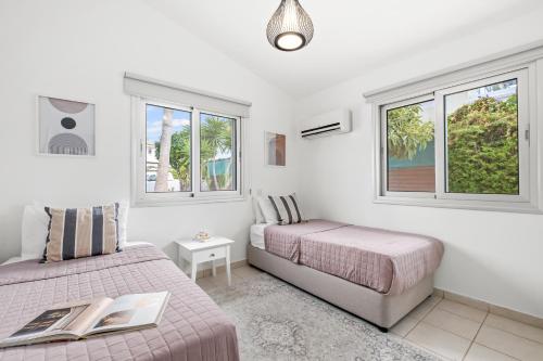 a bedroom with two beds and two windows at Ivy Blue Villa by Nomads - Short Walk to Coral Bay in Peyia