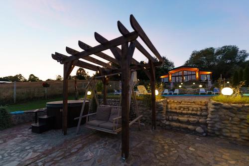 a wooden pergola with a chair next to a stone wall at Balada dintre dealuri - Casa Soarelui si Casa Lunii in Cisnadioara
