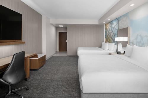 a hotel room with two beds and a desk and a tv at Courtyard by Marriott Clearwater Beach in Clearwater Beach
