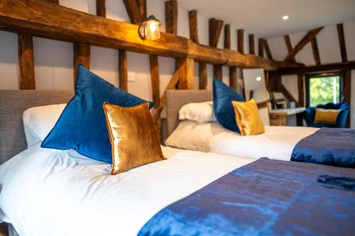 two beds with blue and gold pillows in a room at The Barn at Chart Hills in Biddenden
