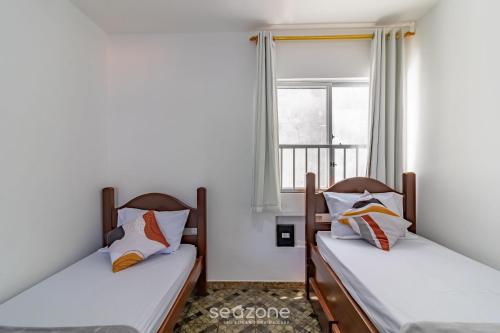 zwei Betten in einem Zimmer mit Fenster in der Unterkunft Apto Aconchegante a 350m da Praia do Forte ECF0306 in Škorak