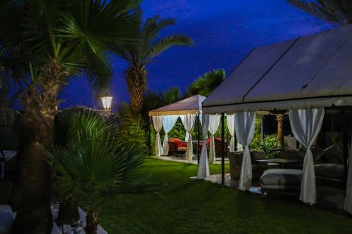 a backyard with white umbrellas and palm trees at night at Weedan Hôtel&Spa Marrakech in Oulad Snaguia