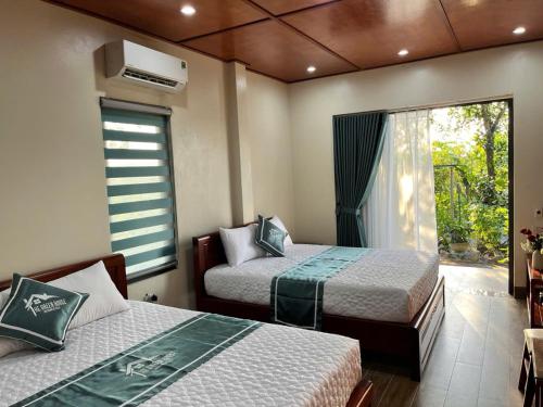 a bedroom with two beds and a window with a fan at The Green House Homestay in Ninh Binh