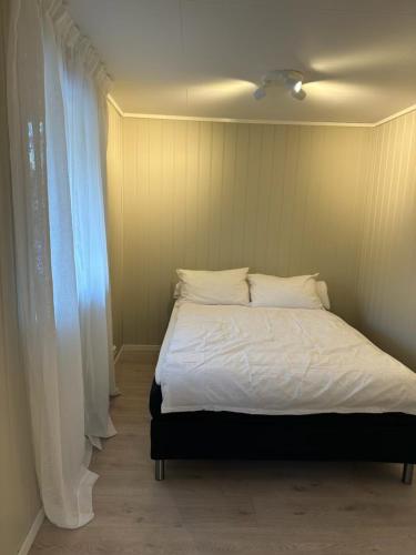 a bed with white sheets and pillows next to a window at Lys rent og trivelig hybelleilighet in Kristiansand