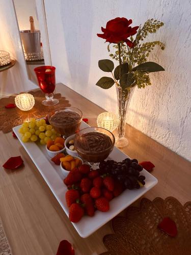 a plate of fruit on a table with a vase of roses at Hotel Netto in Cachoeiras de Macacu