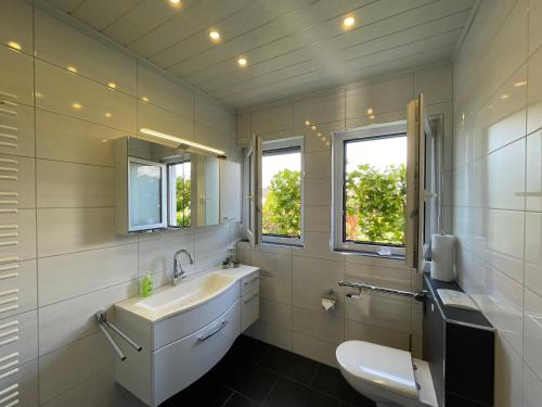 a bathroom with a sink and a toilet and two windows at Pension Braun - Dein Ankerplatz in Löhne