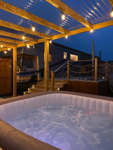 a hot tub on a deck with a rv in the background at Horse Truck Tiny Home with Hot Tub in Ashbourne