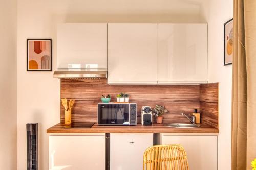 une cuisine avec des armoires blanches et un micro-ondes dans l'établissement La Suite Soleil - Maison studio avec jardin privé, à Décines-Charpieu