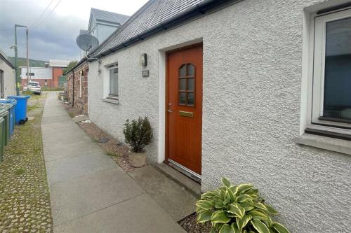 a white house with a brown door and a sidewalk at Pebble Cottage in Golspie