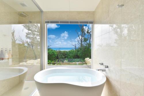 ein weißes Bad mit einer Badewanne und einem Fenster in der Unterkunft Feliz Villa Suite Miyakojima Ueno in Miyako-jima
