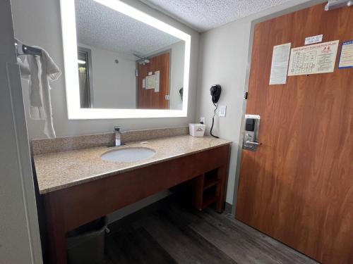 a bathroom with a sink and a mirror and a door at Days Inn by Wyndham Tulsa Central in Tulsa