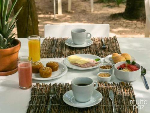 een tafel met bekers en borden met eten en drinken bij Muita Paz Rooms in Atins