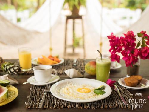 een tafel met borden met ontbijtproducten en -dranken bij Muita Paz Rooms in Atins