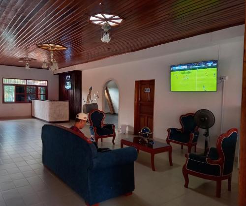 a man sitting on a couch in a living room with a tv at El Jaguar Casa Hotel in Leticia