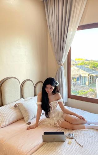 a woman sitting on a bed with a laptop at Homestay Lucie đảo Phú Quý in Cu Lao Thu