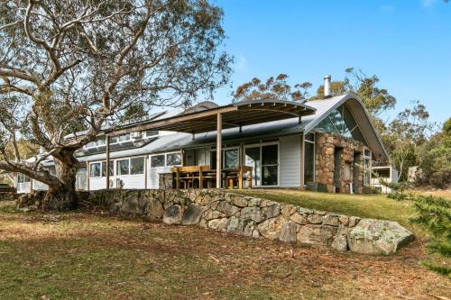a house with a metal roof and a stone wall at Silvertop Chalet in Crackenback