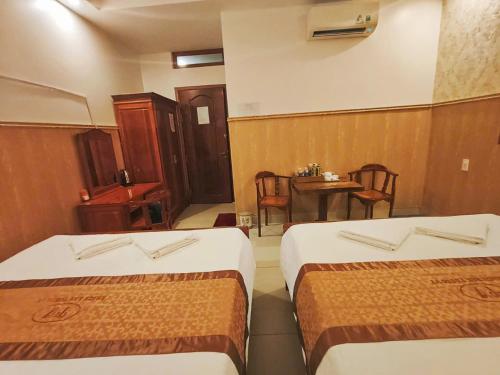 two beds in a room with a table and chairs at Khách Sạn Tường Vy in An HÃ²a