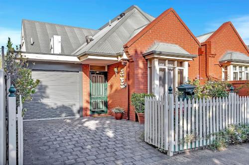 a red brick house with a white fence at Picket Fence Cottage - Steps from Adelaide Oval in North Adelaide