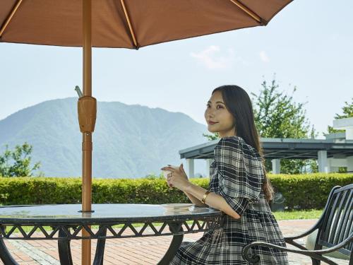 a woman sitting at a table under an umbrella at Hakuba Alps Hotel in Otari