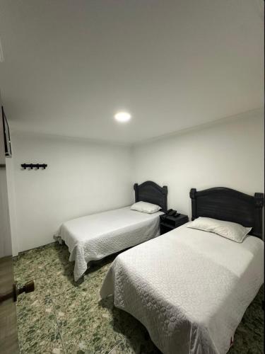 two beds in a room with white walls at Hotel Nuevo Horizonte E.M.J in Bogotá