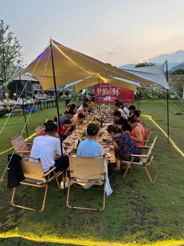 a group of people sitting at a long table under a tent at Zhangjiajie Cliff Flower RV Tent Hotel in Sanguansi