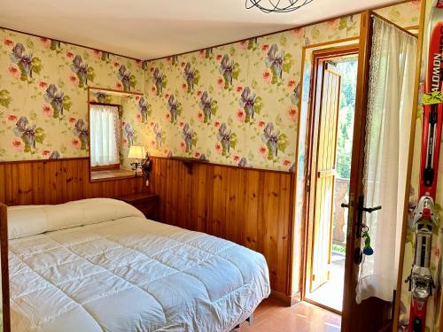Schlafzimmer mit einem Bett mit Blumentapete und einem Fenster in der Unterkunft Cozy Three-Room Apartment with Mountain View & Parking - Ussin Chalet - Valtournenche in Chamois