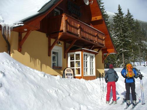 two people on skis in the snow in front of a building at Pension Katty in Špindlerův Mlýn
