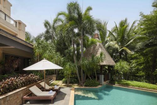 a resort pool with chairs and an umbrella and palm trees at Raffles Hainan Clear Water Bay in Sanya