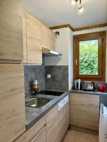 une cuisine avec des armoires en bois, un évier et une fenêtre dans l'établissement Sapins 11 - Appartement familial - Pied des pistes - Vue sur les montagnes, aux Houches