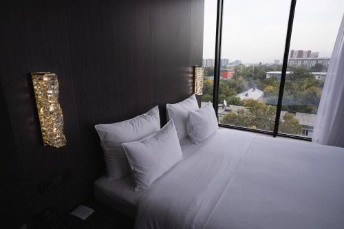 a bedroom with a white bed with a large window at Resident City Hotel in Almaty