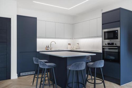 a kitchen with white cabinets and blue island with stools at Modern Brixton Apartments in London