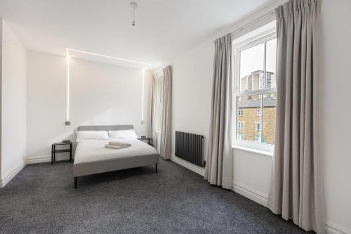 a white bedroom with a bed and a window at Modern Brixton Apartments in London