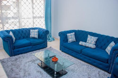 a living room with two blue couches and a glass table at Studio Apartment near the Airport in Nairobi