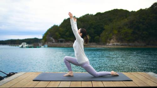 a woman doing a yoga pose on a dock near the water at 船で行く 1日1組限定の絶景宿 うみらぼ in Shima