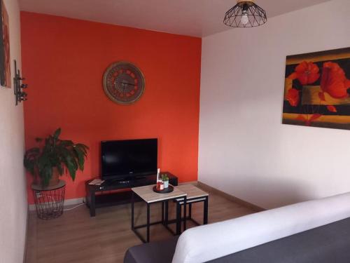 a living room with an orange wall with a tv and a table at Le Camus in Belonchamp