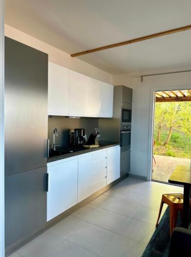 une cuisine avec des placards blancs et une grande fenêtre dans l'établissement ALOES Appartement T3, à Saint-Florent