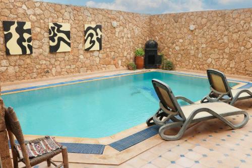 a swimming pool with two chairs and a rock wall at Panoramic View Villa, 4 Bed, Pool in Mirleft
