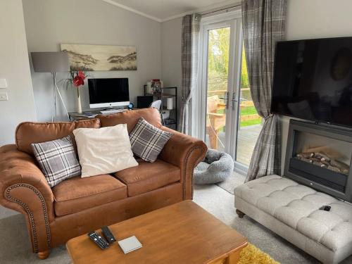 a living room with a brown leather couch and a fireplace at Cosy Clos Y Hendy Lodge in Penbryn
