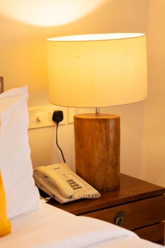 a lamp on a table next to a bed with a phone at Solo Inn By Hawk Hospitality in Cochin