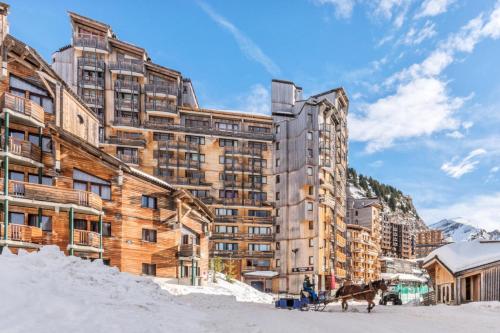 un grand bâtiment dans la neige avec un cheval devant dans l'établissement Résidence Les Alpages - maeva Home - Appartement 2 pièces 4 personnes - Sélection MAE-0171, à Avoriaz