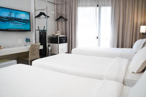 a hotel room with three beds and a desk and a tv at Radisson Rio de Janeiro Barra in Rio de Janeiro