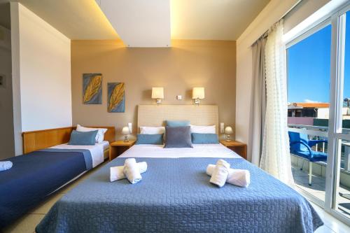 two beds in a room with a large window at RODI BLUE apartments in Amoudara Herakliou