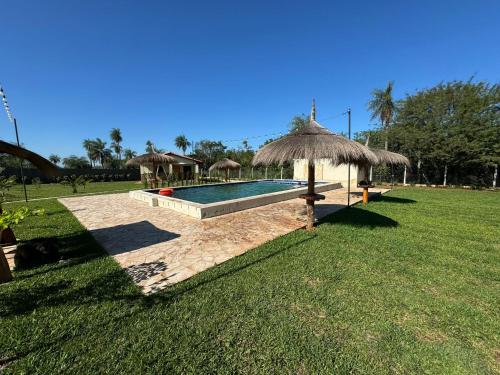 una piscina con ombrellone di paglia accanto a un campo di Residencia Piri a Piribebuy