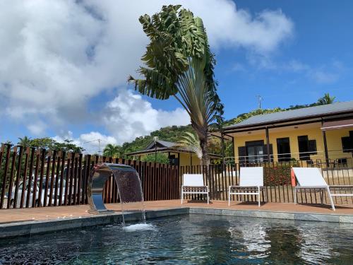 a pool with a fountain with two chairs and a palm tree at Lodges Balourou in Montjoly