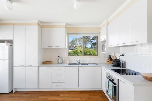 a white kitchen with white cabinets and a window at Leura on Ophir in Ventnor