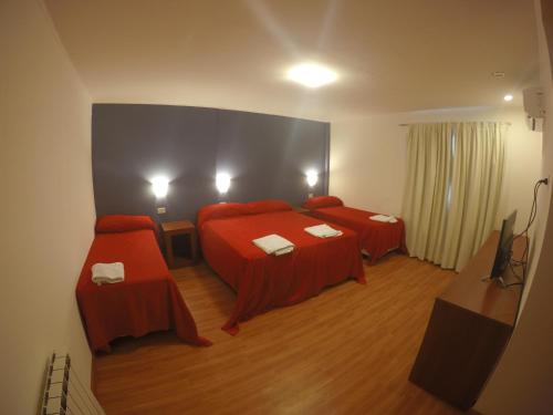 Habitación con 2 camas con sábanas rojas y TV. en Hotel Torrevado en Las Grutas